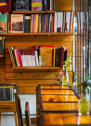 Ambiente en Marabunta. Mesa y silla de madera, frente a una ventana, con un estante lleno de libros al fondo.